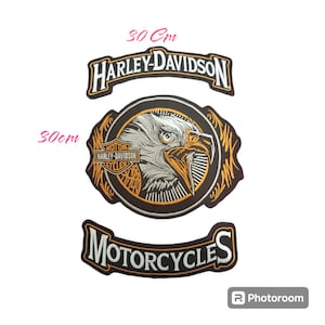 Könnte beinhalten: Drei Harley-Davidson Motorrad-Patches. Der obere Patch ist schwarz mit weißem Text, der in einem geschwungenen Banner "Harley-Davidson" lautet. Der mittlere Patch ist schwarz mit einem silbernen Adlerkopf in einem Kreis mit goldenen Akzenten. Der untere Patch ist schwarz mit weißem Text, der in einem geschwungenen Banner "Motorcycles" lautet.