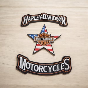 May include: Three embroidered patches featuring the Harley-Davidson logo. The top patch is black with orange stitching and reads "Harley-Davidson". The middle patch is a red, white and blue star with the Harley-Davidson logo in the centre. The bottom patch is black with orange stitching and reads "Motorcycles".