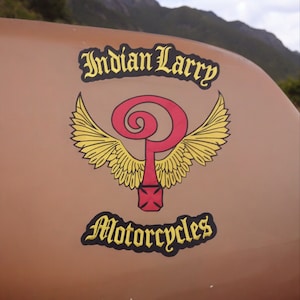 May include: A brown motorcycle gas tank with a yellow and red logo that says "Indian Larry Motorcycles" with a stylized winged symbol.