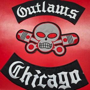 Puede incluir: Parches bordados en blanco y negro con el texto "Outlaws" y "Chicago" en una fuente gótica. Un cráneo con ojos rojos y pistones cruzados está en el centro.