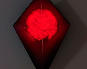 Può includere: Una lampada da parete a forma di diamante che emette un vivido bagliore rosso. L'apparecchio presenta un design geometrico sfaccettato con un punto di illuminazione centrale circolare che si irradia verso l'esterno, creando un motivo sulla superficie rossa scura.