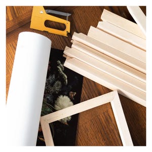 K&ouml;nnte beinhalten: Kunstbedarf, darunter eine gelbe Tackerpistole, eine Rolle wei&szlig;e Leinwand, Holzkeilrahmenleisten und ein teilweise montierter Holzrahmen. Die Artikel sind auf einer Holzoberfl&auml;che angeordnet.