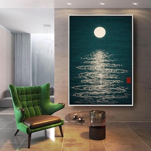 Può includere: Una stampa artistica incorniciata raffigura una scena notturna serena. Una luna piena illumina l'acqua increspata, creando un sentiero scintillante. L'opera presenta uno sfondo verde acqua scuro con un timbro rosso nell'angolo in basso a destra. Una poltrona verde e un tavolo di vetro sono in primo piano.