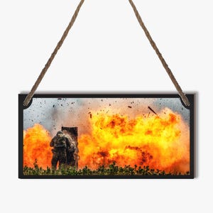 May include: A rectangular sign with a black border and a rope hanger. The image depicts a military scene with soldiers and a large explosion of orange and yellow flames. The background shows a cloudy sky and green foliage.