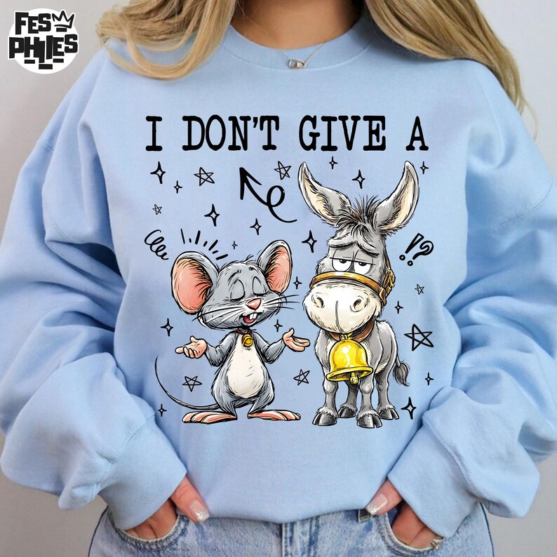 May include: Light blue sweatshirt with a graphic of a mouse and a donkey. The mouse has its arms out, and the donkey has a bell around its neck. The text "I DON'T GIVE A" is above the characters.