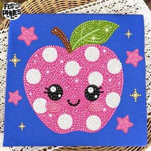Peut inclure: Une toile carrée bleue présentant une mosaïque de diamants en forme de pomme rose à pois blancs, avec une feuille verte et une tige brune. La pomme a un visage souriant aux grands yeux noirs et joues roses, entourée d'étoiles roses et d'éclats jaunes.