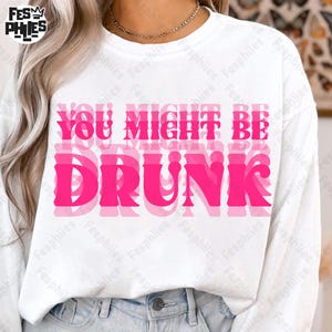 Puede incluir: Sudadera blanca de manga larga con la frase "YOU MIGHT BE DRUNK" en letras rosas superpuestas. La sudadera tiene cuello redondo y está hecha de un material suave. El diseño está centrado en la parte delantera.