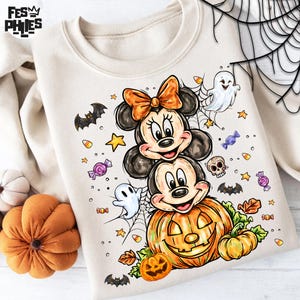 Puede incluir: Sudadera crema con un dise&ntilde;o de Halloween. El dise&ntilde;o incluye a Mickey y Minnie Mouse, una calabaza tallada, fantasmas, murci&eacute;lagos, caramelos y una telara&ntilde;a. Los personajes est&aacute;n apilados sobre una calabaza.