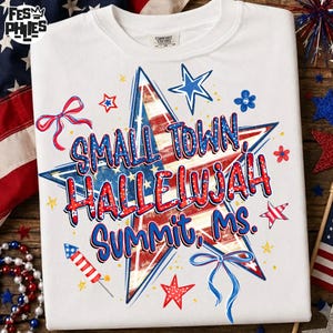 Puede incluir: Una camiseta blanca con un gráfico de estrella grande en el centro con un patrón rojo, blanco y azul. El texto dice "SMALL TOWN, HALLELUJAH SUMMIT, MS." en letras azules y rojas. El diseño incluye estrellas pequeñas, un cohete y cintas azules.