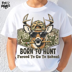 Pode incluir: Uma t-shirt branca com um gráfico de um veado usando um boné de basebol camuflado e óculos de sol pretos, segurando um lápis amarelo na boca. O design inclui um fundo camuflado e o texto BORN TO HUNT Forced To Go To School.