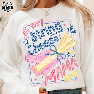May include: White sweatshirt with a colorful graphic that reads "In my String Cheese Mama Era." The design features a bundle of yellow string cheese tied with a blue ribbon, set against a pink and blue frame.