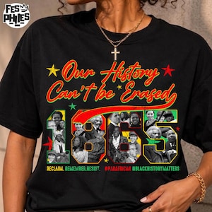 Op de afbeelding: Een zwart t-shirt met de rood, geel en groen gekleurde tekst Our History Can't be Erased boven het getal 1865. Het ontwerp bevat een collage van historische zwarte figuren, kleine sterren en de tekst RECLAIM, REMEMBER, RESIST, #PANAFRICAN, #BLACKHISTORYMATTERS.
