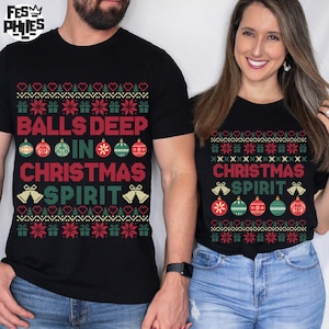 May include: Black t-shirts with a Christmas-themed design. The shirts feature the text "BALLS DEEP IN CHRISTMAS SPIRIT" and "CHRISTMAS SPIRIT" in a festive font, along with ornaments and bells.