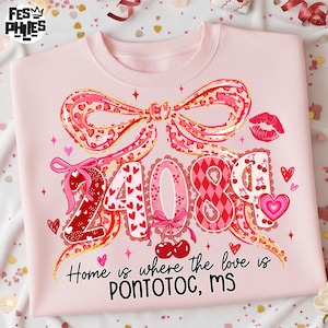 Puede incluir: Una sudadera rosa claro con un gran lazo y los números "2408" en una fuente decorativa. El diseño incluye corazones, cerezas y el texto "Home is where the love is PONTOTOC, MS."