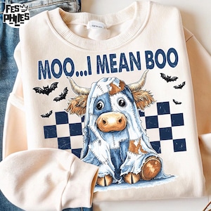 May include: Cream-colored sweatshirt with a Halloween-themed graphic. The design features a cow dressed as a ghost with the text "MOO...I MEAN BOO" in navy blue. Black bats and a navy blue and white checkered pattern complete the design.