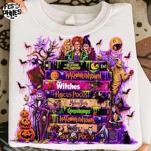 May include: A white crewneck sweatshirt featuring a graphic print of stacked VHS tapes labeled with movie titles including The Nightmare Before Christmas, Halloweentown, The Witches, Hocus Pocus, The Addams Family, Goosebumps, and Wolf.