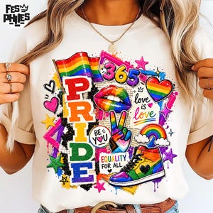 May include: A cream-colored t-shirt featuring a vibrant graphic print with the word PRIDE in vertical rainbow letters, a rainbow flag, a peace sign hand, a high-top sneaker, a rainbow heart, and the text 365, love is love, BE YOU, and EQUALITY FOR ALL.