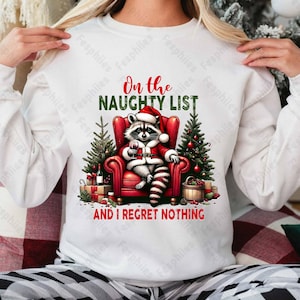 May include: White sweatshirt with a red and green Christmas design featuring a raccoon wearing a Santa hat and holding a glass of wine. The text reads "On the Naughty List and I Regret Nothing".