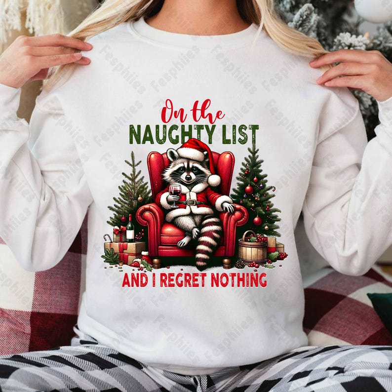 May include: White sweatshirt with a red and green Christmas design featuring a raccoon wearing a Santa hat and holding a glass of wine. The text reads "On the Naughty List and I Regret Nothing".