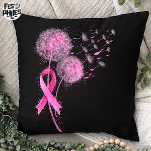 May include: Black square pillow featuring a pink ribbon and two pink dandelions with seeds blowing in the wind. The pillow is a decorative item, likely for a bed or couch.