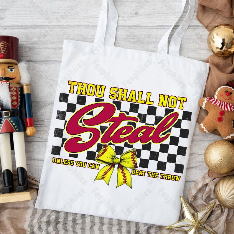 May include: White tote bag with a black and white checkered background. The text "Thou Shall Not Steal Unless You Can Beat The Throw" is printed in red and black. A yellow softball with a bow is in the center of the bag.