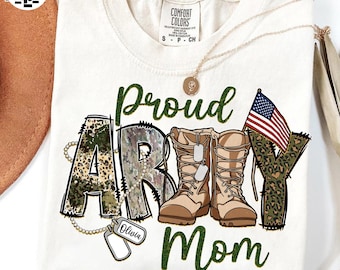 May include: A white t-shirt with a green and brown camouflage print that says "Proud Army Mom". The shirt also features a small American flag and a dog tag with the name "Olivia" on it.