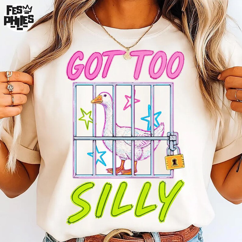 May include: Cream-colored t-shirt with the text "GOT TOO SILLY" in pink and green. A cartoon goose is inside a cage with stars. The cage has a padlock.