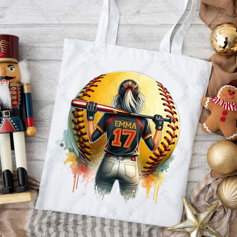 May include: White tote bag with a watercolor design of a softball player with the name "Emma" and the number "17" on the back of their jersey.