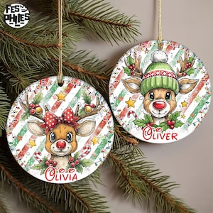 May include: Two round Christmas ornaments featuring reindeer designs. One reindeer wears a red bow, the other a green hat. Both have red noses and candy canes. The ornaments are decorated with holly, stars, and a striped background.
