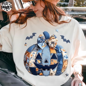 Puede incluir: Sudadera crema con un dise&ntilde;o de calabaza patchwork en tonos azules, naranjas y estampados florales. La calabaza tiene una cara sonriente y est&aacute; adornada con un lazo. Murci&eacute;lagos y estrellas tambi&eacute;n est&aacute;n en la camisa.