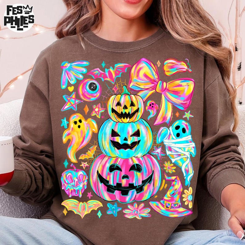 May include: Brown sweatshirt featuring a colorful Halloween-themed graphic. The design includes stacked jack-o'-lanterns, ghosts, bats, and a witch's hat, all in vibrant neon colors. The sweatshirt has a crew neck and long sleeves, perfect for the fall season.