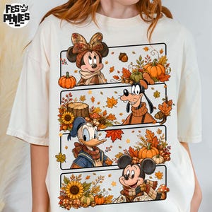 Puede incluir: Una camiseta de color crema con un estampado gráfico dividido en cuatro paneles horizontales. Los paneles muestran personajes de dibujos animados como Minnie Mouse, Goofy, el Pato Donald y Mickey Mouse rodeados de hojas de otoño, calabazas y girasoles.