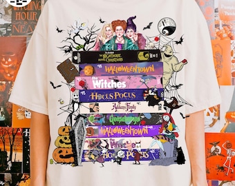 May include: Cream-colored t-shirt featuring a stack of Halloween-themed books with illustrations of characters from popular movies. The books include titles like "The Nightmare Before Christmas," "Hocus Pocus," and "Goosebumps." Black bats and other spooky elements are scattered around the books.