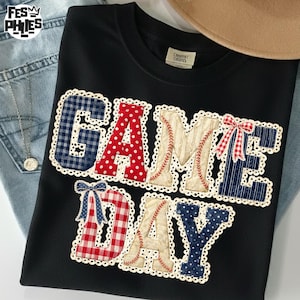 Puede incluir: Sudadera negra con la frase "GAME DAY" en un diseño de patchwork. Las letras presentan varios patrones, incluyendo cuadros, lunares y costuras de béisbol, con lazos decorativos. Un tema casual y deportivo.