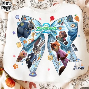 May include: White sweatshirt featuring characters from the animated film "Zootopia 2". The design includes a large blue bow with various characters and the film's logo. The sweatshirt has a crew neck and long sleeves.