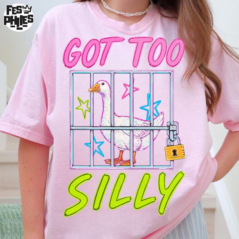 May include: Pink t-shirt with a graphic of a white goose inside a cage, with the words "GOT TOO SILLY" in pink and green. The goose has an orange beak and feet. The cage has a padlock.