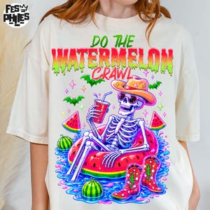 Peut inclure: Un t-shirt blanc cassé avec un motif représentant un squelette portant un chapeau de cowboy et des lunettes de soleil, assis dans une bouée pastèque. Le texte indique DO THE WATERMELON CRAWL. Le design inclut de l'eau, des tranches de pastèque.