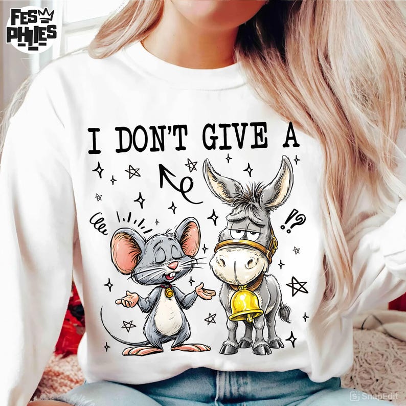 May include: White sweatshirt with the text "I DON'T GIVE A" above a cartoon illustration of a mouse and a donkey. The mouse is gray with pink ears, and the donkey is gray with a gold bell.
