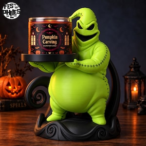 May include: A lime green, sack-like figure with black stitched details holding a black circular candle holder. The holder contains a cylindrical candle with a black label featuring orange pumpkins, bats, and the text Pumpkin Carving Autumn Night Candle.
