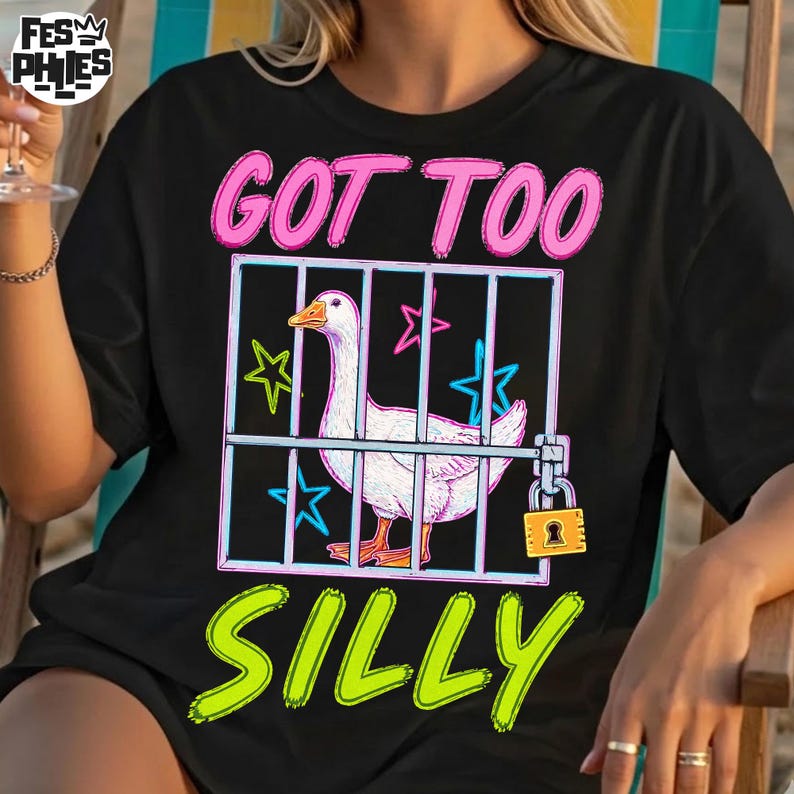 May include: Black t-shirt with a graphic of a white goose inside a cage, the text "GOT TOO SILLY" in pink and green. The cage has a padlock and star accents.