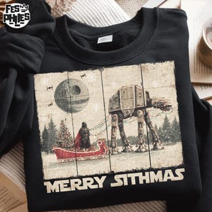 Könnte beinhalten: Schwarzes Sweatshirt mit einem festlichen Star Wars-Design. Die Grafik zeigt Darth Vader in einem Schlitten, der von einem AT-AT gezogen wird, mit dem Todesstern im Hintergrund. Der Text "MERRY SITHMAS" ist unter dem Bild aufgedruckt.