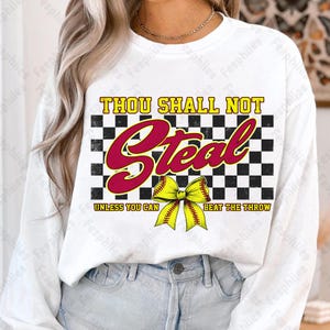May include: White long-sleeve shirt with a black and white checkered background. The text "Thou Shall Not Steal Unless You Can Beat The Throw" is printed in red and black. A yellow softball with a red bow is in the center of the design.