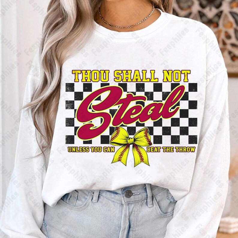 May include: White long-sleeve shirt with a black and white checkered background. The text "Thou Shall Not Steal Unless You Can Beat The Throw" is printed in red and black. A yellow softball with a red bow is in the center of the design.