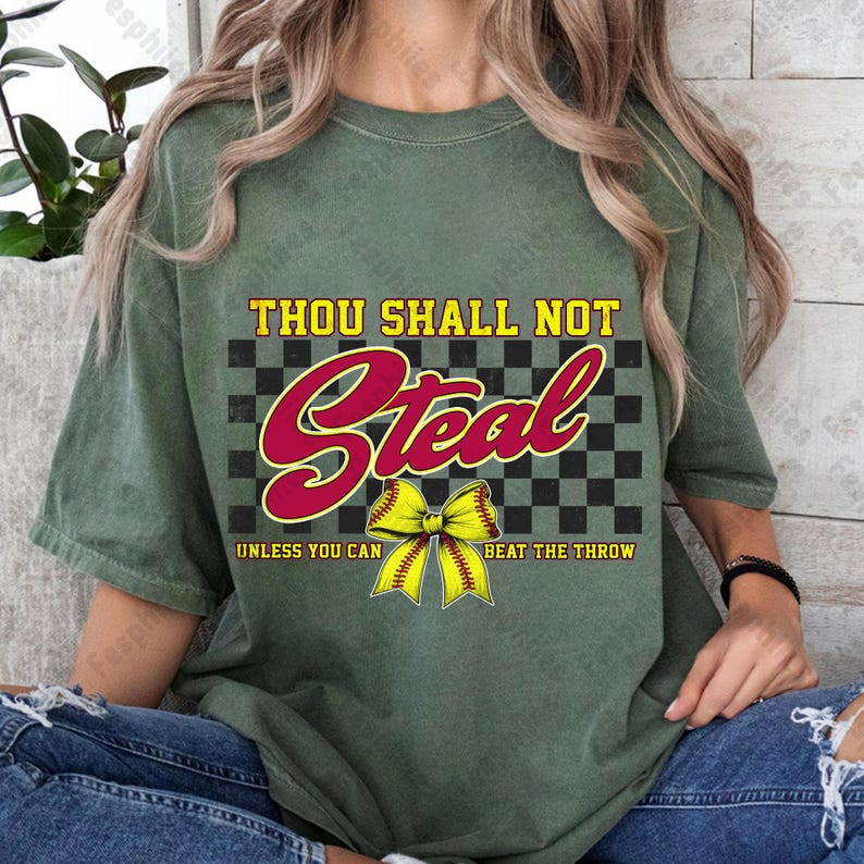 May include: Green t-shirt with a black and white checkered background and the text "Thou Shall Not Steal" in red. A yellow softball with a red bow is in the center of the design. The text "Unless You Can Beat The Throw" is below the softball.