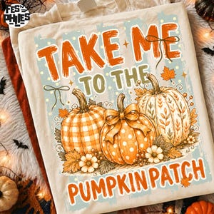 May include: A cream-colored t-shirt featuring a graphic of three pumpkins with orange and white patterns, including gingham and polka dots. The text reads "TAKE ME TO THE PUMPKIN PATCH" in orange lettering, accented with small orange leaves and bows.