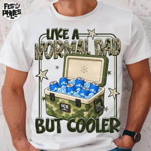 May include: A white t-shirt featuring a graphic of a camouflage-patterned cooler filled with blue beverage cans and ice. The text reads LIKE A NORMAL DAD BUT COOLER. The design includes star accents and a small snowflake icon on the cooler lid.