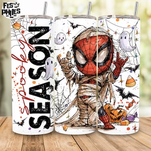 May include: A cylindrical tumbler with a metal straw featuring a cartoon character wrapped in bandages like a mummy, spiderwebs, bats, ghosts, candy corn, and pumpkins. The text "SPOOKY SEASON" is printed in large black and red script lettering.