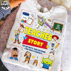 May include: White sweatshirt featuring colorful cartoon characters and the words "Teacher Story." The design includes images of a jar of stars, Buzz Lightyear, Woody, Jessie, and other Toy Story characters. The text "To Infinity and Beyond for Our Students" is also included.