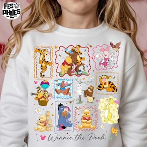 May include: White sweatshirt featuring colorful cartoon illustrations of Winnie the Pooh and friends. The design includes characters like Tigger, Piglet, and Eeyore, with the words "Winnie the Pooh" printed at the bottom.