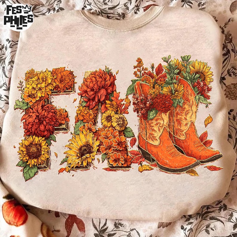 May include: Beige sweatshirt featuring a "FALL" design in autumnal colours. The letters are filled with sunflowers and chrysanthemums. Two orange cowboy boots are filled with flowers. The design has a fall theme.